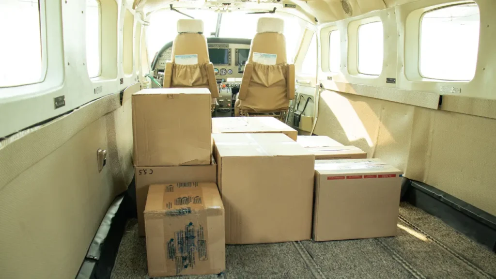 Carga aérea ou transporte rodoviário: qual escolher? Pequenas caixas acomodadas dentro de um avião confrontando carga aérea ou transporte rodoviário